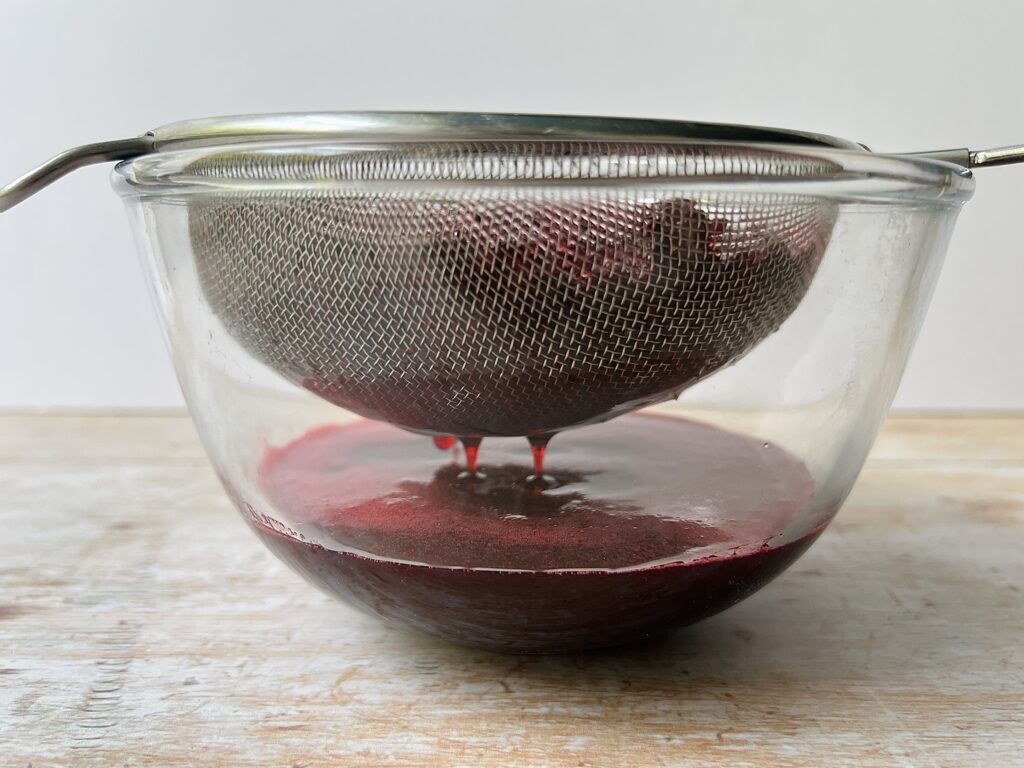 straining bramble shrub mixture through a sieve