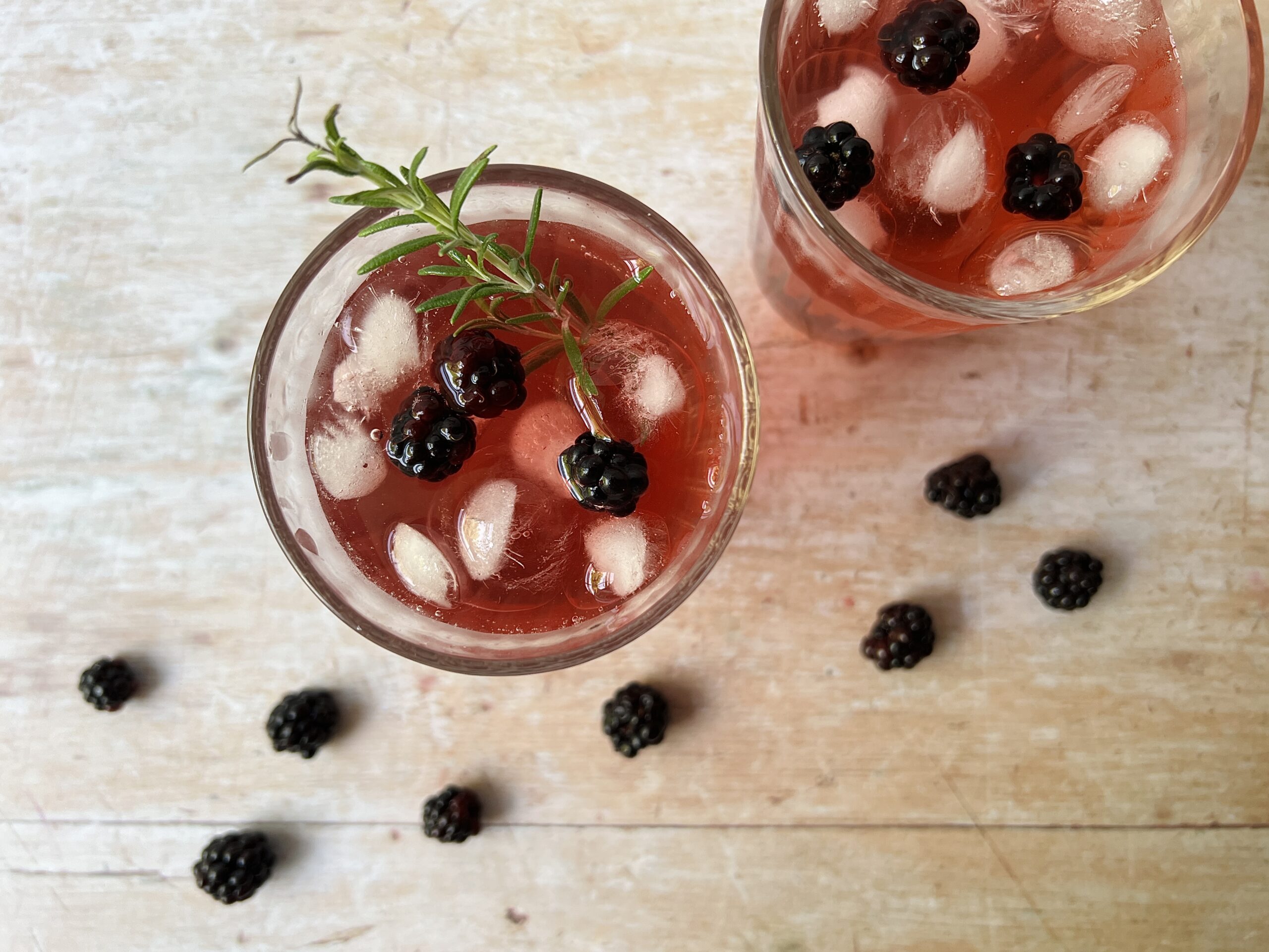 two glasses of bramble shrub drink with rosemary