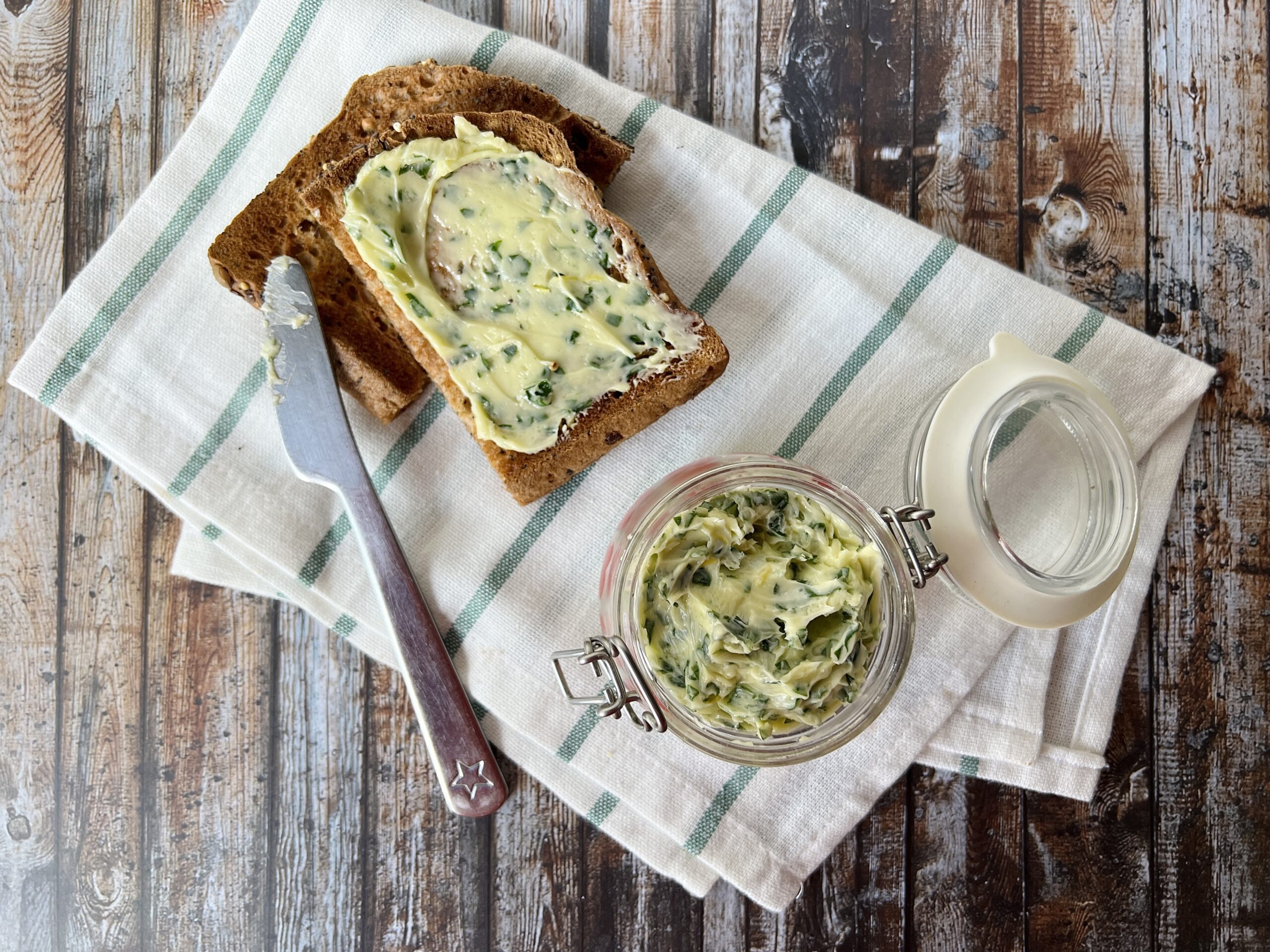 A tea towel with a jar of wild garlic butter on top of it, alongside two slices of toast with garlic butter.