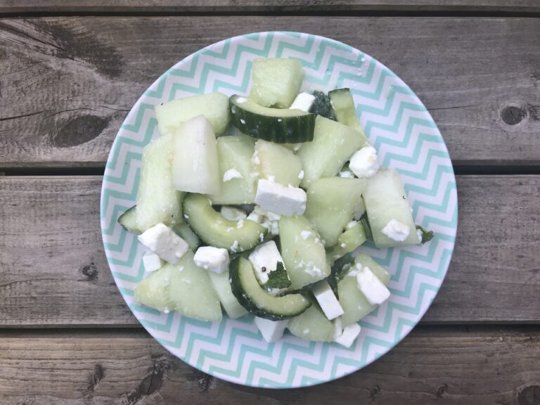 A plate with a portion of salad made up of honeydew melon, cucumber and feta cheese.